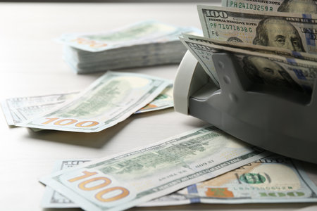 Money counter machine with dollar banknotes on white wooden table, closeupの写真素材