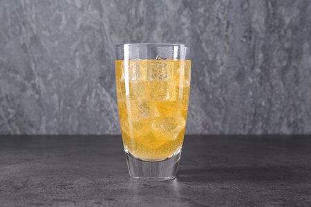 Sweet soda water with ice cubes in glass on grey table