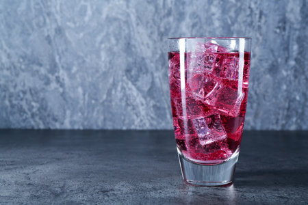 Sweet soda water with ice cubes in glass on grey table, space for textの写真素材