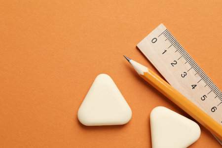 Erasers, ruler and pencil on orange background, flat lay. Space for textの写真素材