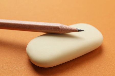 Eraser and pencil on orange background, closeup