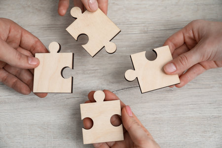 Teamwork. Group of people putting puzzle pieces together at wooden table, top viewの写真素材