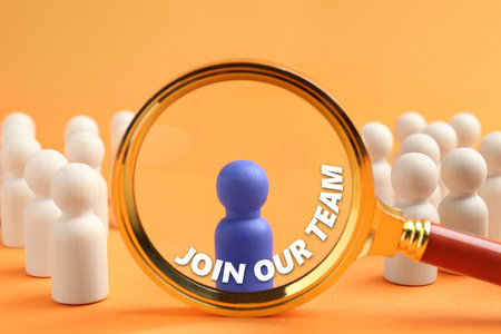 Join Our Team announcement. Blue figure among wooden ones on orange background, view through magnifying glass. Human resourceの写真素材