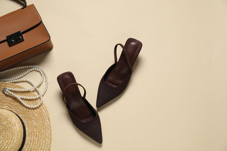 Stylish brown shoes, straw hat, bag and pearl necklace on beige background, flat lay. Space for textの写真素材