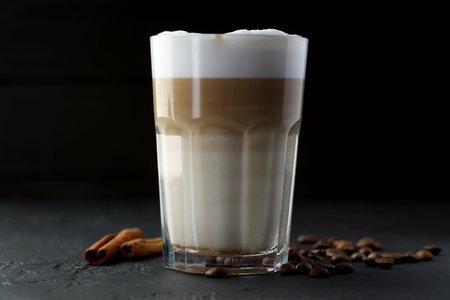 Tasty latte macchiato in glass, coffee beans and cinnamon on black table, closeupの写真素材