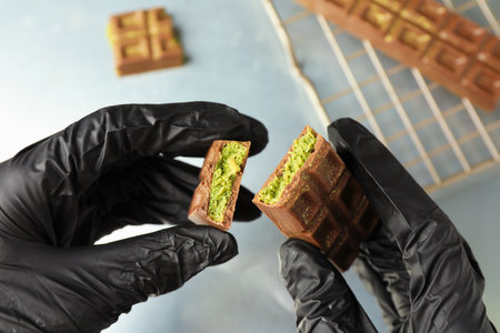 Woman holding pieces of tasty chocolate with pistachios and knafeh at grey table, closeupの写真素材