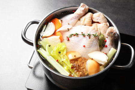 Whole fresh turkey, cut onion, carrot, celery, spices in pot and stove on grey table, closeupの写真素材
