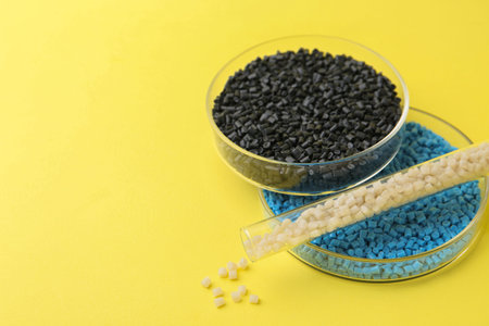 Colorful plastic granules in petri dishes and test tube on yellow background, closeup. Space for...