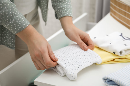 Woman folding baby clothes at home, closeup