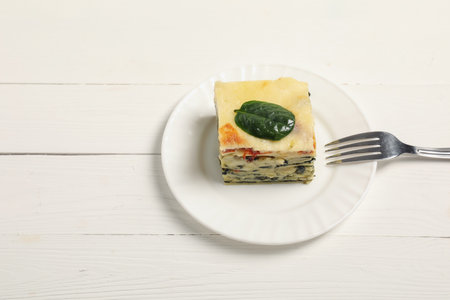 Piece of spinach lasagne and fork on white wooden tableの写真素材