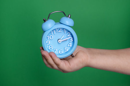 Child holding light blue alarm clock on green backgroundの写真素材