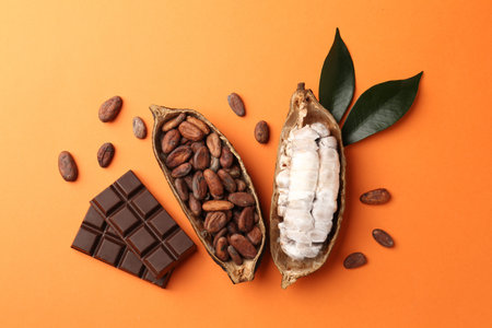 Cocoa pods with beans and chocolate on orange background, flat lay