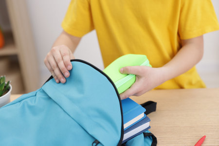 Boy packing backpack for school at wooden table indoors, closeupの写真素材