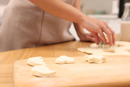 Woman cutting out cookies at wooden table indoors, closeup