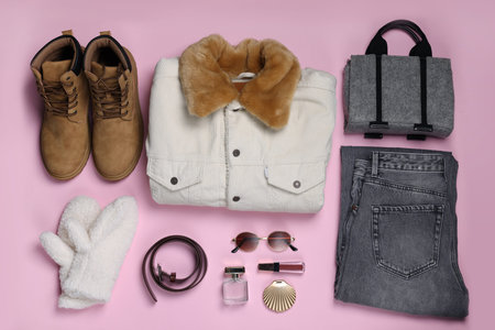 Stylish outfit with warm jacket and accessories on light pink background, flat lay