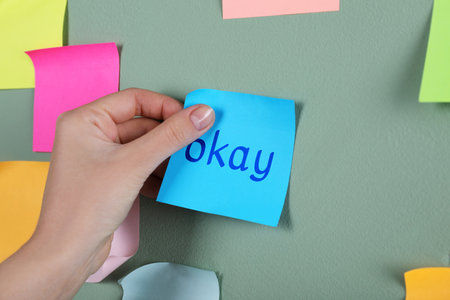 Woman sticking note with word Okay on color wall, closeupの写真素材