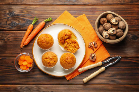 Tasty carrot muffins, fresh vegetables, and walnuts on wooden table, flat layの写真素材