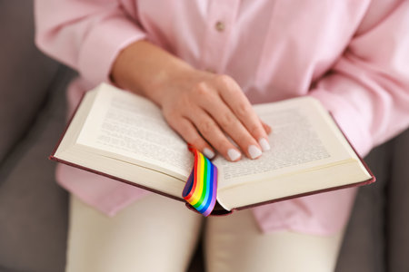 Woman with ribbon in LGBT colors reading book indoors, closeupの写真素材