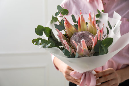 Woman with beautiful bouquet against light wall, closeup