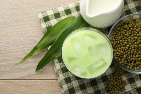 Fresh mung bean juice with ice in glass, milk, leaves and seeds on wooden table, flat layの写真素材