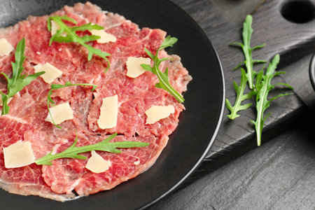 Fresh beef carpaccio with arugula and cheese on dark textured table, closeupの写真素材