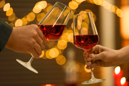 Couple clinking glasses of wine against blurred lights, closeup. Romantic dinnerの写真素材