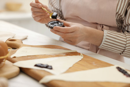 Woman with jam and fresh dough at white table indoors, closeup. Making croissantsの写真素材