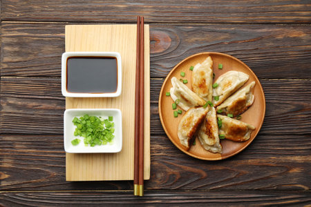 Delicious fried gyoza dumplings with green onions served on wooden table, flat lay