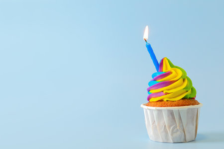 Tasty cupcake with colorful cream and burning candle on light blue background, space for textの写真素材