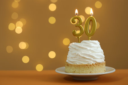 30th birthday. Cupcake with burning number shaped candles on table against golden background with blurred lights, closeup and space for text. Bokeh effectの写真素材