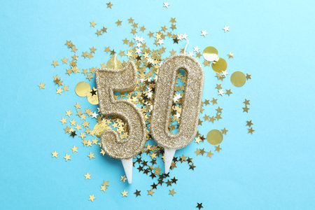 50th birthday. Number shaped candles and confetti on light blue background, flat layの写真素材