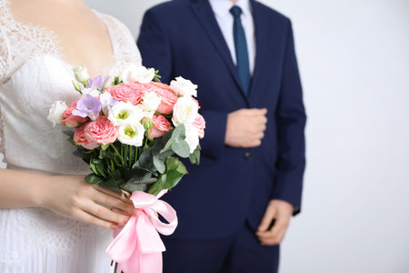 Bride with beautiful wedding bouquet and groom on light background, closeup. Space for textの写真素材