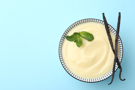 Tasty vanilla pudding, mint and pods on light blue background, top view. Space for textの写真素材