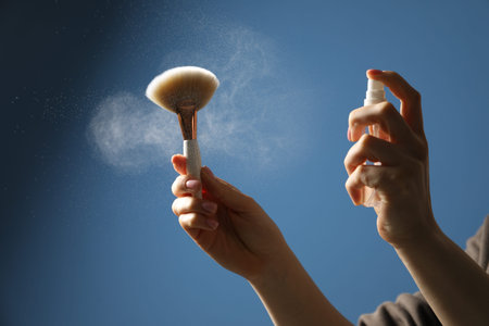 Woman cleaning makeup brush with spray on blue background, closeupの写真素材