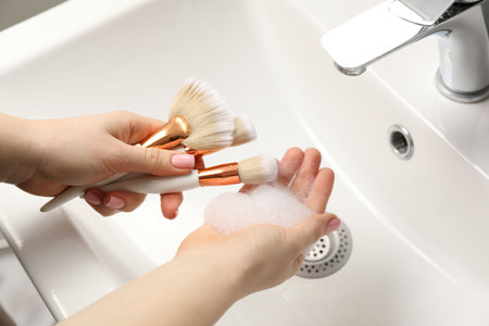 Woman washing makeup brushes with soap over sink, closeupの写真素材