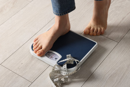 Woman on scales and measuring tape indoors, closeup.