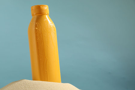 Bottle of sun protection product on sand against light blue background, space for textの写真素材