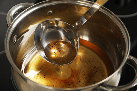 Pouring used cooking oil from ladle into saucepan, closeupの写真素材