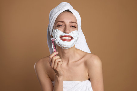 Happy woman shaving facial hair with razor on brown backgroundの写真素材