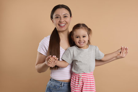 Portrait of happy mother and her cute little daughter on beige backgroundの写真素材