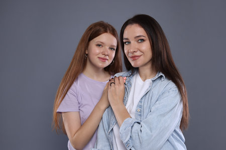 Portrait of beautiful mother with teenage daughter on grey backgroundの写真素材