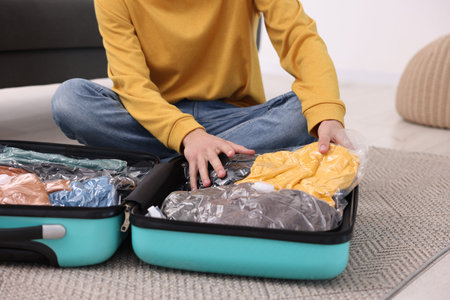 Man packing clothes into vacuum bag on floor indoors, closeup