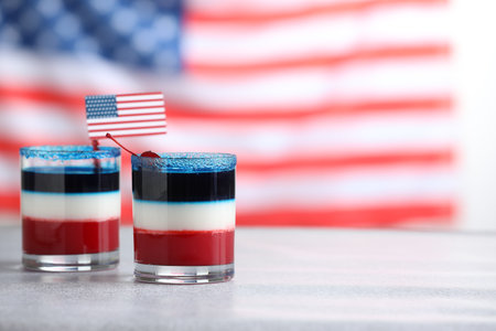 Tasty cocktails in glasses with small paper flag of USA on table against blurred background, space for textの写真素材