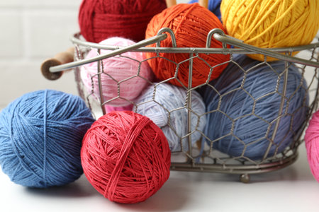 Balls of colorful yarn in metal basket on white wooden table, closeupの写真素材