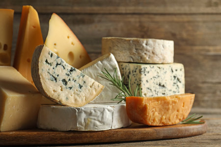 Different types of cheese and rosemary on wooden table, closeup
