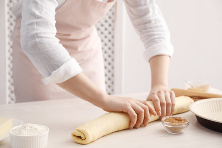 Making cinnamon rolls. Woman shaping dough at white wooden table, closeupの写真素材