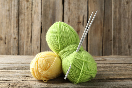 Skeins of colorful yarn and knitting needles on wooden table, closeupの写真素材