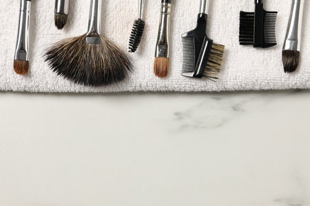 Clean makeup brushes with towel on white marble table, top view. Space for textの写真素材