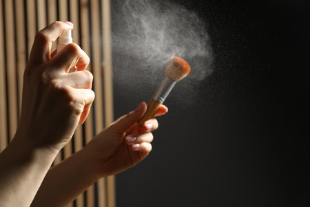Woman cleaning makeup brush with spray indoors, closeup. Space for textの写真素材