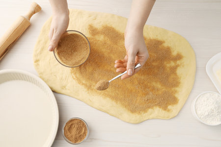 Making cinnamon rolls. Woman adding spice, with sugar into dough at white wooden table, top view